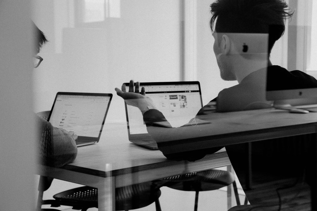 Zwei Personen sitzen jeweils mit einem Laptop an einem Tisch in einem Meetingsraum